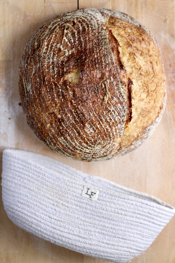 sourdough loaf and banneton basket on wooden surface